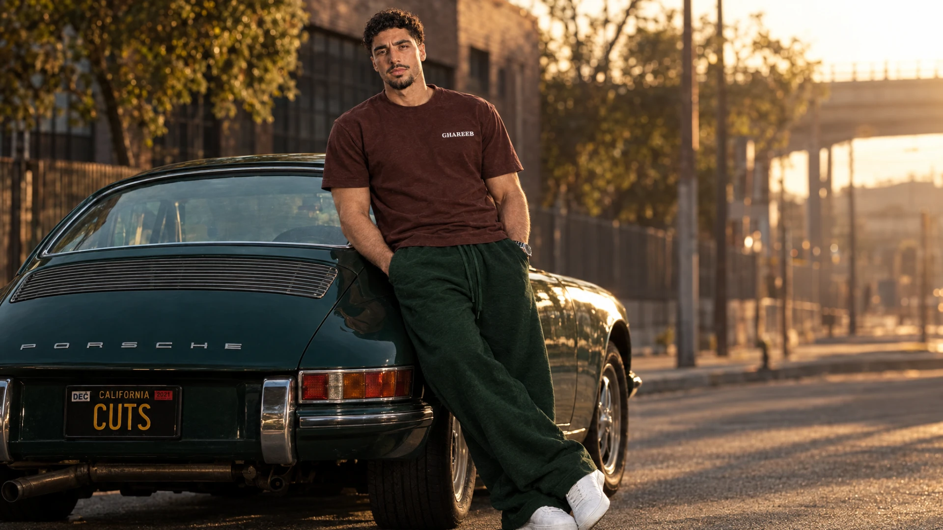 GHAREEB model wearing a brown T-shirt and green sweatpants beside a vintage car